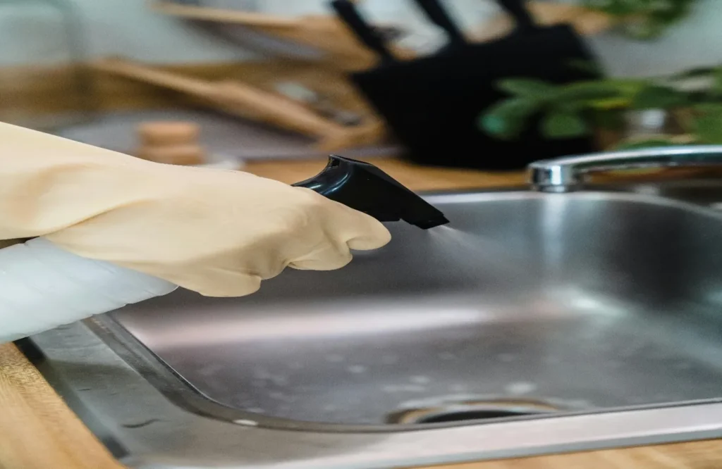 A person in rubber gloves washing a kitchen sink pipeline with a scrub brush