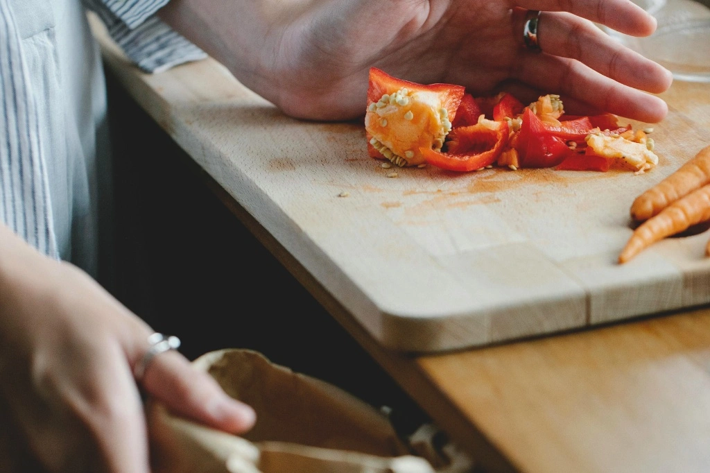 A person is trying to create compost from kitchen waste which he collects on a cutting board by cutting fresh vegetables.