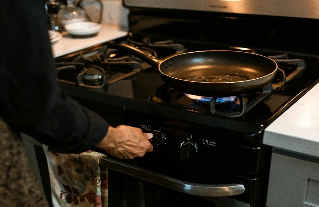 A person holding a frying pan on top of a stove and highlighting the health risks of working in a kitchen.