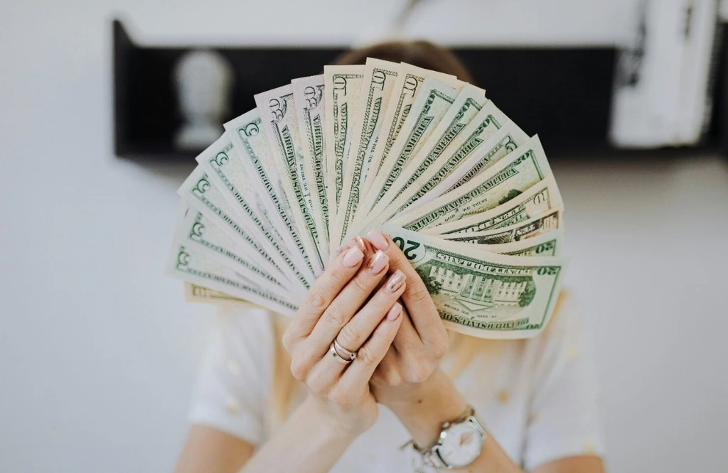 A woman displays money in front of her face, representing the importance of budgeting for kitchen cabinet expenses.