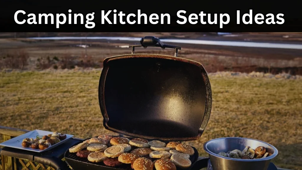 Outdoor camping kitchen setup with a grill, burgers, buns, and mushrooms against a lake and grassy field backdrop.