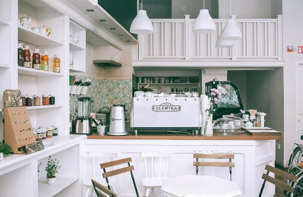 A cozy coffee shop featuring white walls and shelves was designed with thoughtful kitchen layout considerations for efficiency.