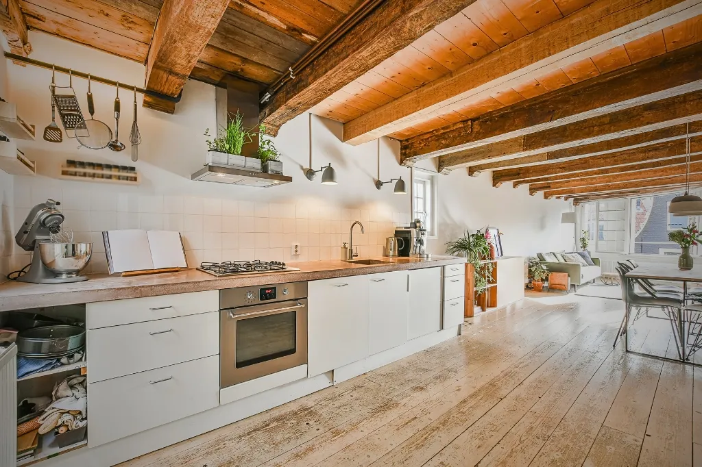 A wide kitchen adorned with wooden beams and white cabinets, creating a bright and open space ideal for culinary activities.