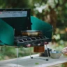 Outdoor setup of a Coleman Powerhouse LP 2-Burner Stove by a camper, showing how to organize a camping kitchen.