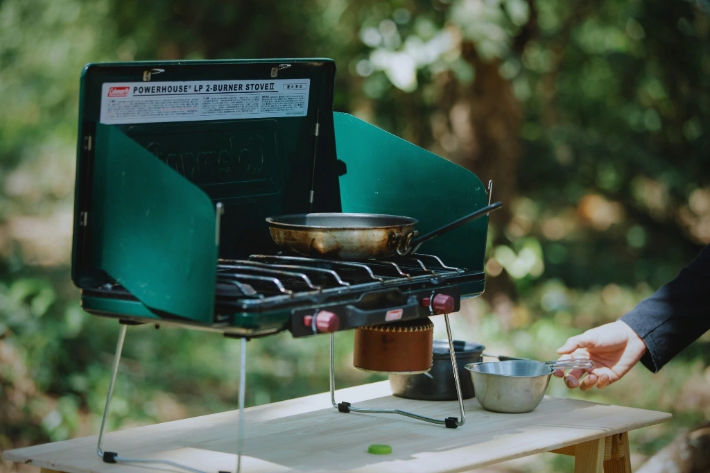 Outdoor setup of a Coleman Powerhouse LP 2-Burner Stove by a camper, showing how to organize a camping kitchen.