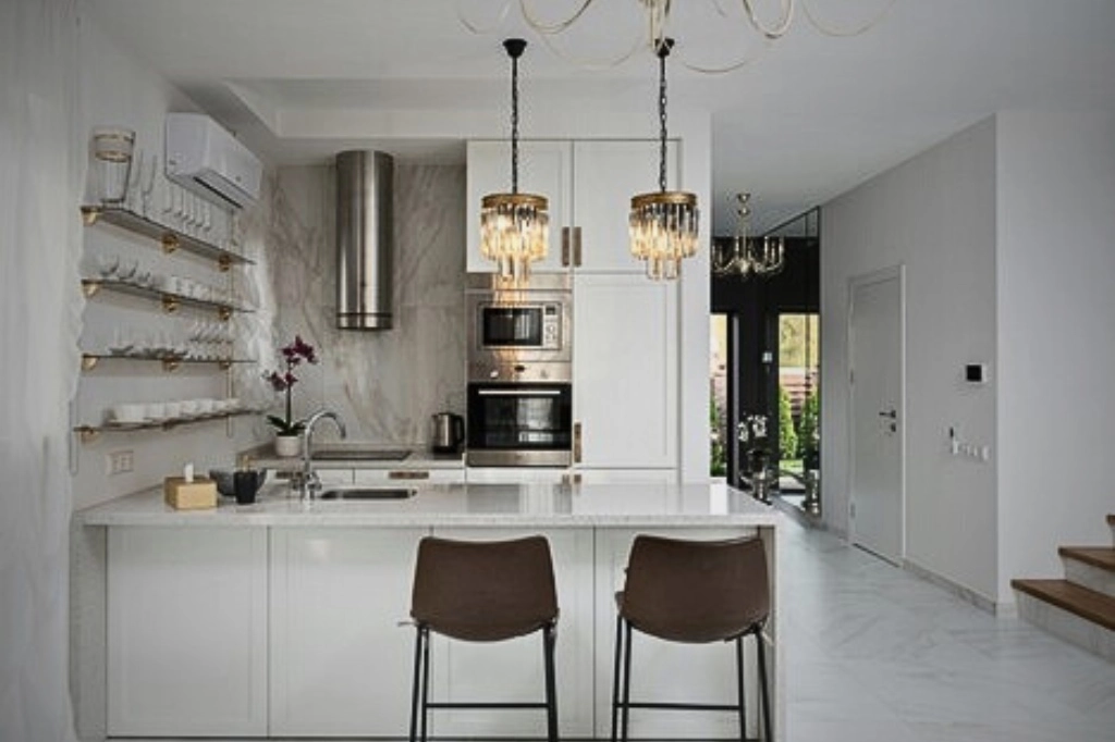 An elegant kitchen with a white countertop, a chandelier, and a design that contrasts open shelving with traditional cabinets.