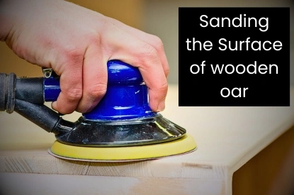 A person sanding the surface of a wooden oak oar, creating a smooth finish for better performance on the water.