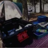 Camping equipment, including a tent, cooler, and portable power station, is set up near a lake, showcasing how to pack kitchen items.