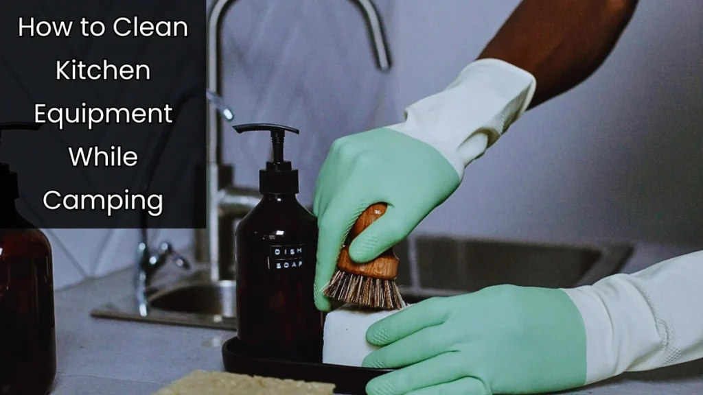 A person wearing green gloves cleaning a dish brush with dish soap near a sink, demonstrating how to clean kitchen equipment while camping.