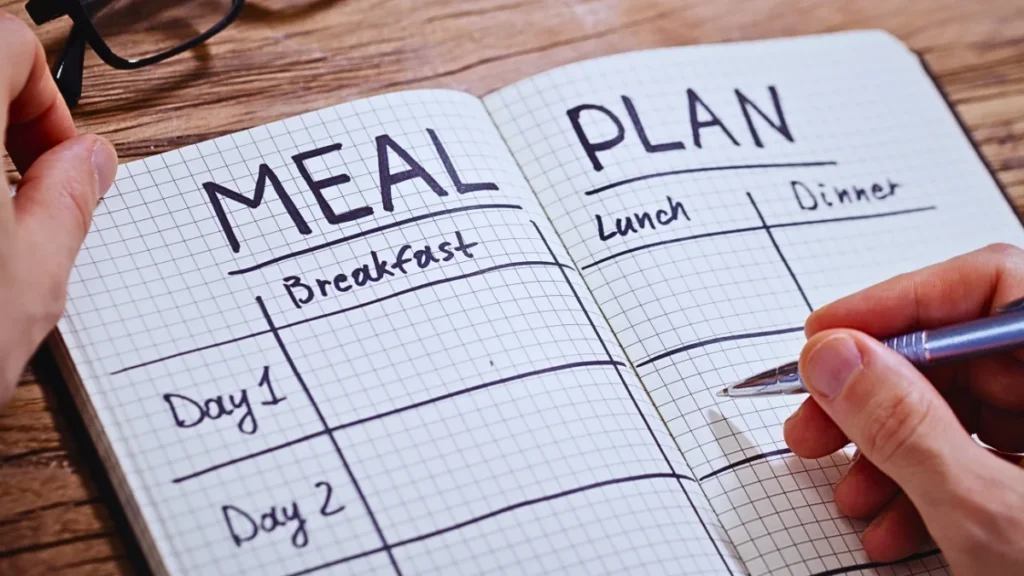 Planning meals in a notebook for a camping kitchen, ensuring well-prepared meals outdoors.