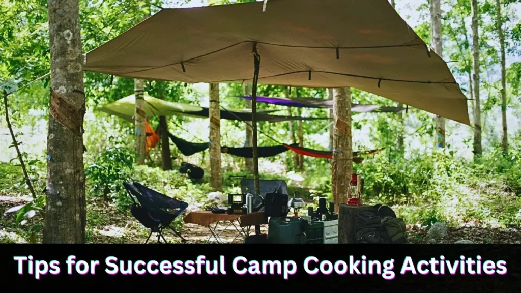 Campsite in a forest with a tarp providing shade, hammocks hanging between trees, and camping supplies arranged on a table.