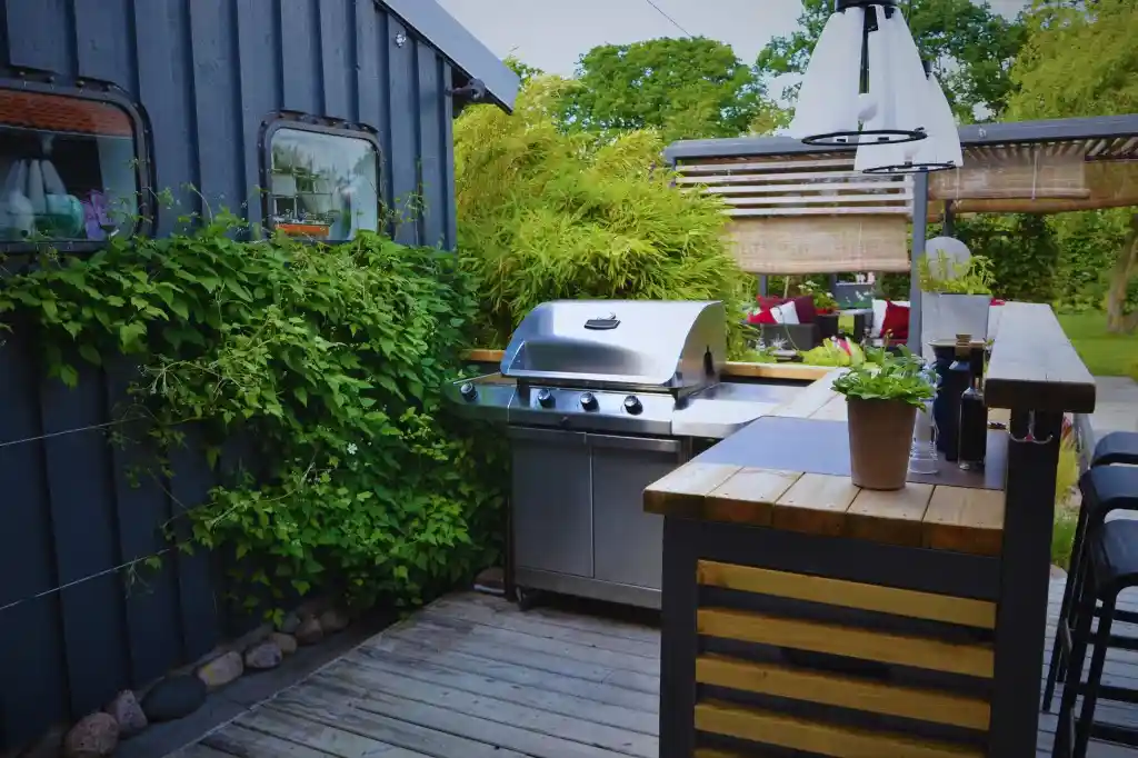 An outdoor kitchen featuring a stainless steel grill, wooden countertop, and lush greenery.