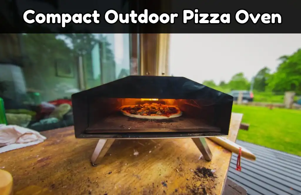 A compact outdoor pizza oven baking a pizza on a wooden table, with a lush green backyard in the background, and a pizza peel beside the oven.