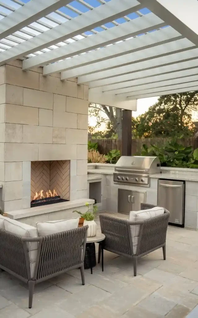 Outdoor kitchen with a built-in fireplace, stainless steel grill, seating area, and pergola, creating a cozy and functional cooking space.