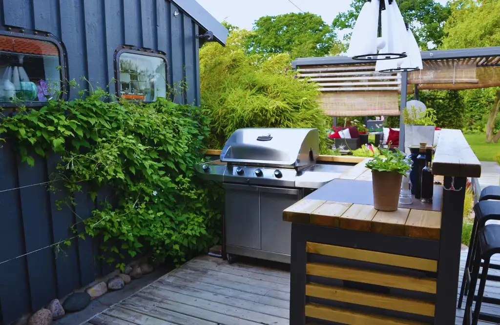 A modern outdoor kitchen featuring a grill, wooden countertop, and surrounding greenery.