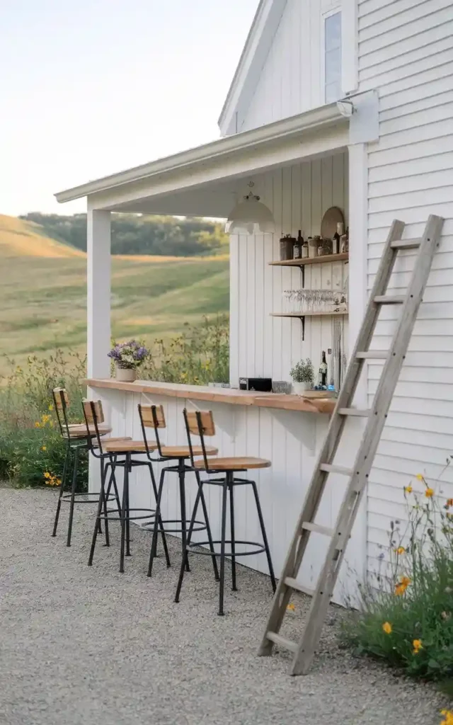 Rustic farmhouse-style outdoor bar with high stools, a wooden ladder, and beautiful flowers.