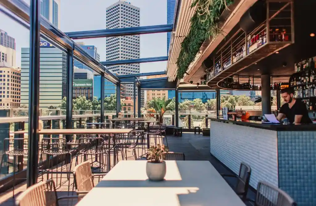 Modern rooftop outdoor kitchen bar with scenic city views, stylish seating, and lush greenery.